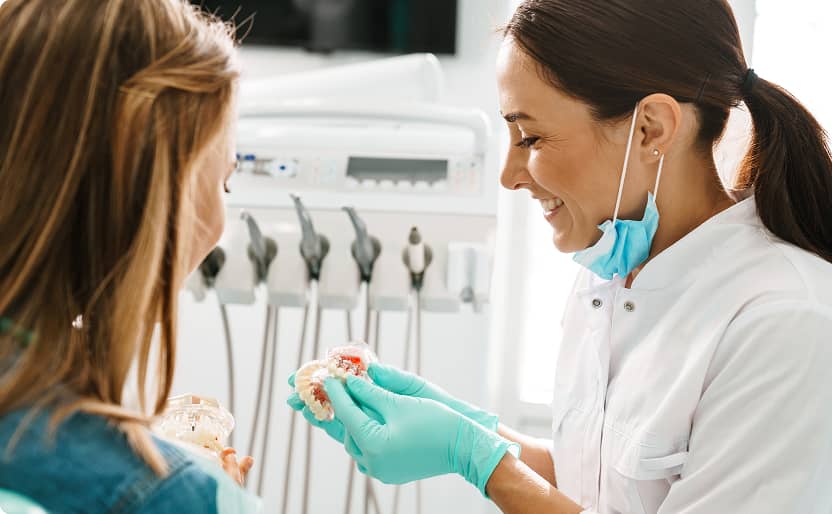 Warragul Smiles Dental | Dentist smiling while showing a young patient a dental model during a consultation
